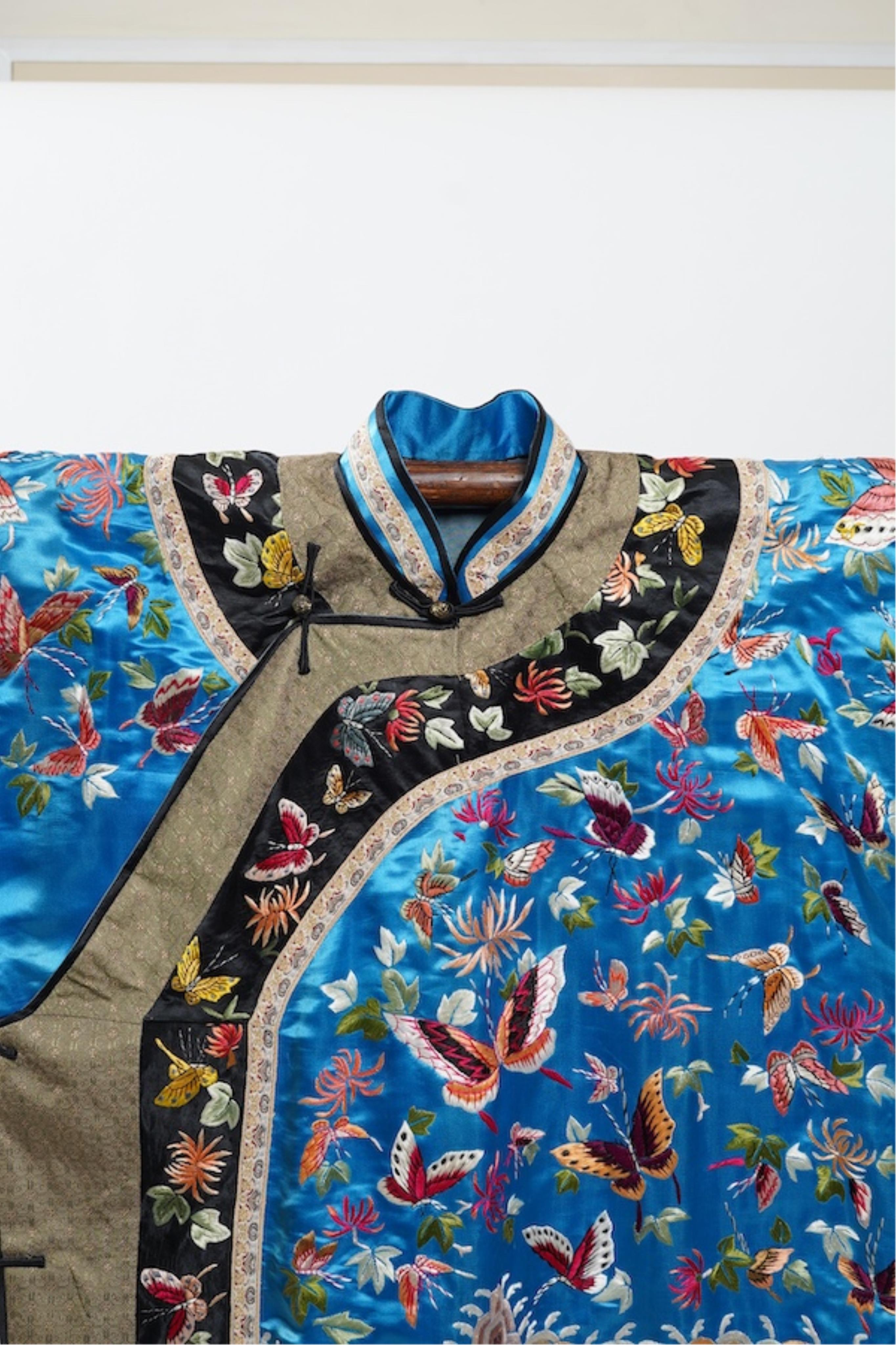 A mid 20th century Chinese turquoise silk jacket, with all over polychrome butterfly embroidery, similar embroidered sleeve bands, front and bottom edges on black silk, all bordered with gold brocade. The jacket blue sil